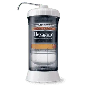 The image features a water purifier labeled "Hexagon™ Water System." It is an 8-stage water purifier, characterized by its transparent cylindrical design that allows the various filtration stages to be visible. The top has a white cap with a spout extending from it, and the base is also white. The filtration layers inside the purifier include different colored materials, indicating the multiple stages of filtration within the system.